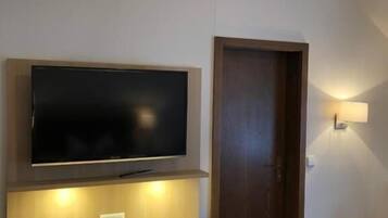 Ein Hotelzimmer mit einem an einer Holzkassette befestigten Flachbildfernseher, einer kleinen Mülltonne, einer Tür und einer wandmontierten Leuchte.