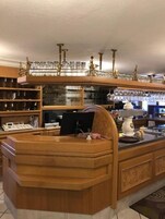 Zona de bar con estantes de madera que sostienen vasos y botellas, una caja registradora y un monitor de computadora.