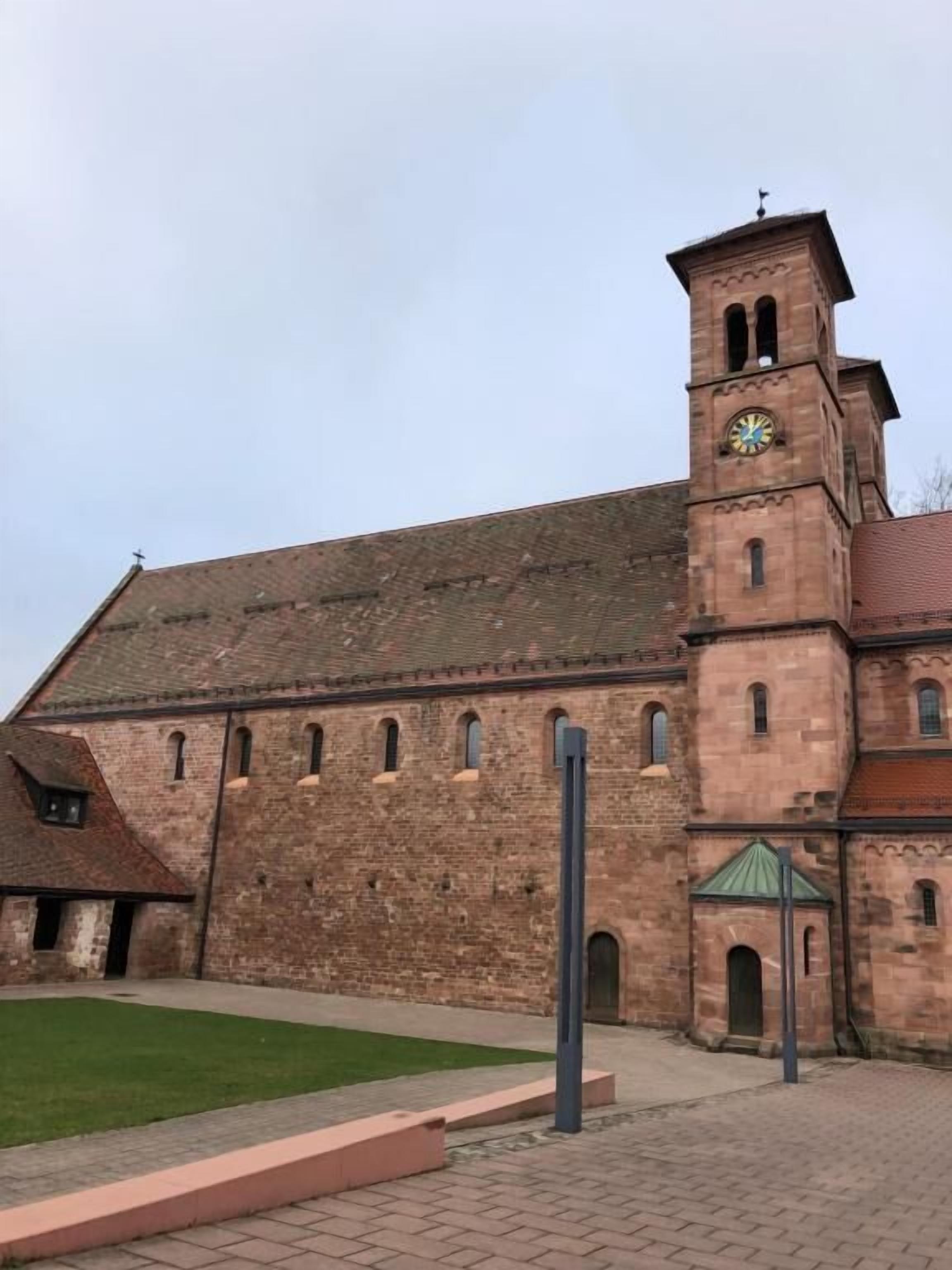 Ein historisches Backsteingebäude mit einem Glockenturm, einem grünen Rasen und einem gepflasterten Weg.