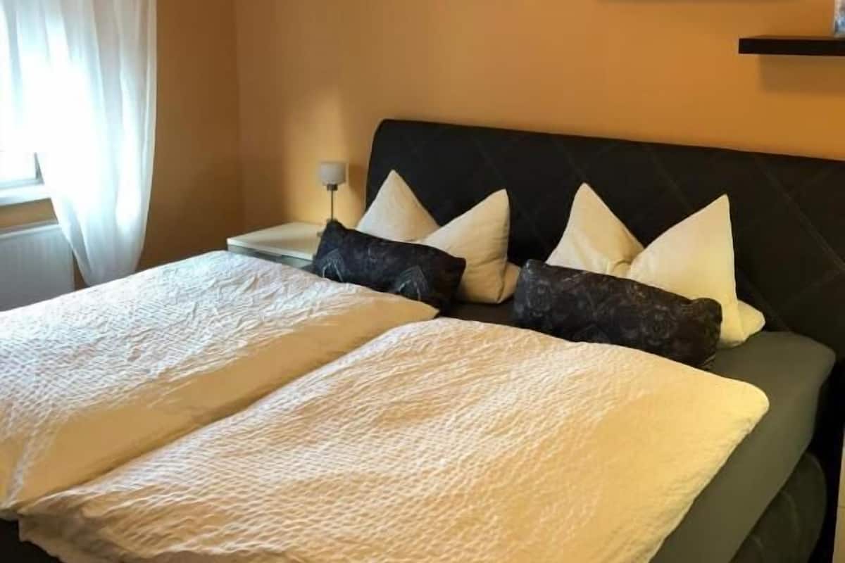 A bed with a quilted cover, a headboard, and multiple pillows.