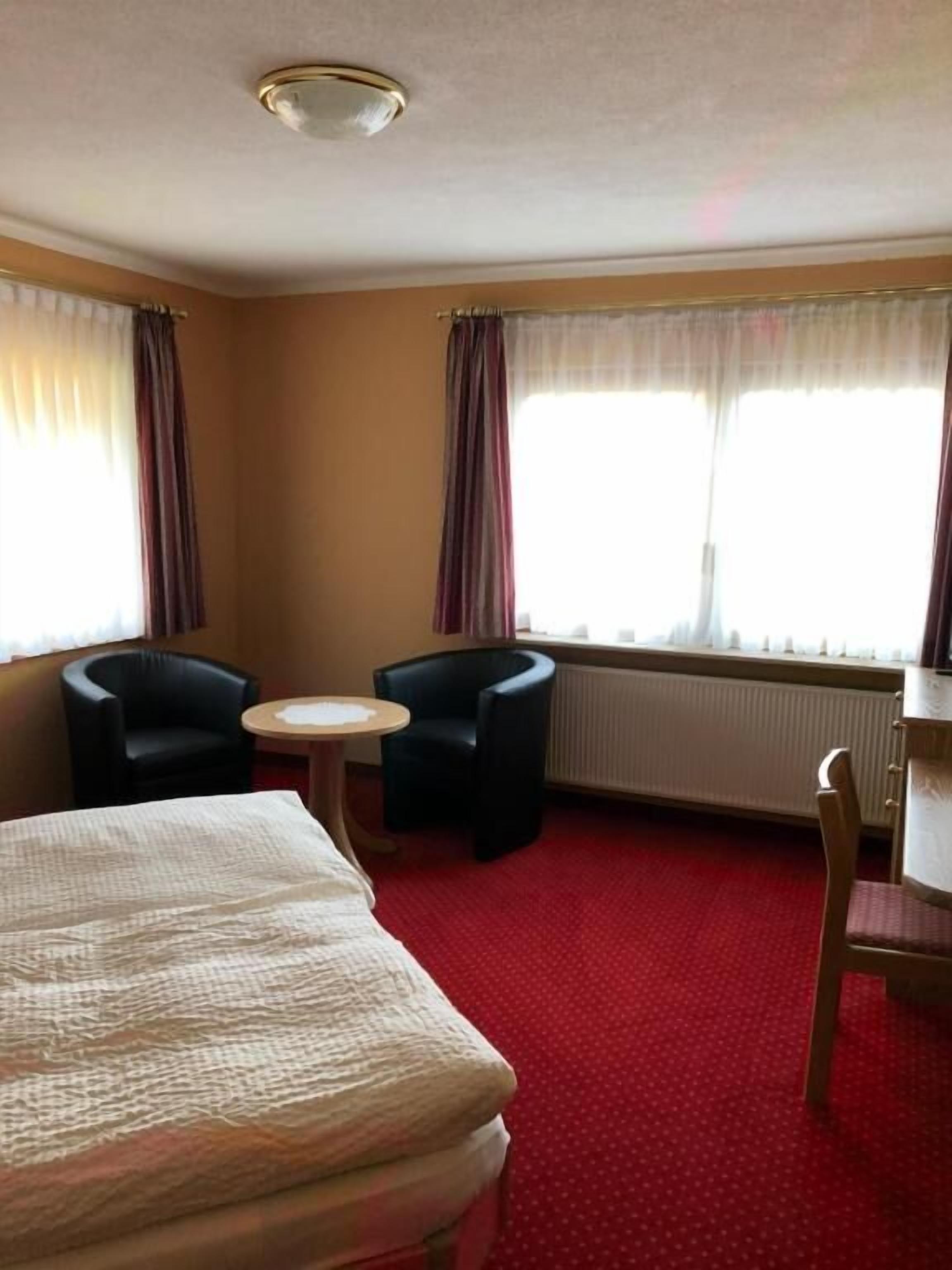 Et hotelværelse med seng, to stole, et lille rundt bord og en radiator.