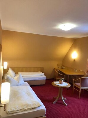 A hotel room with two beds, a small round table with a lamp, a chair, and a desk. - HOTEL ZUM SCHÜTZEN  (Baiersbronn)