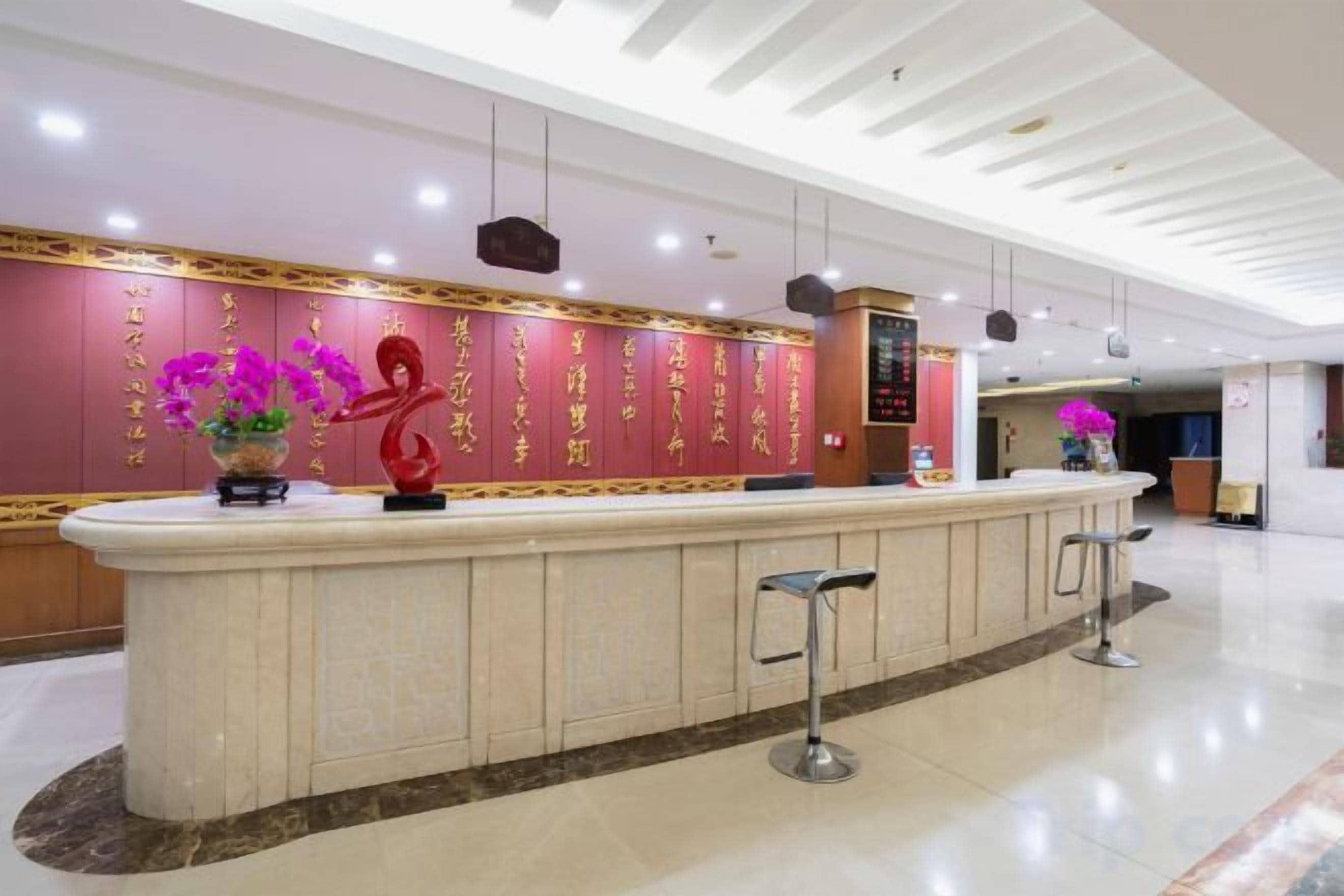 Un espace d’accueil doté d’un comptoir en marbre, d’une sculpture rouge et d’un mur orné d’inscriptions dorées.