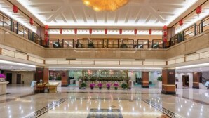 A spacious lobby with a central floral display, a high ceiling with a decorative light fixture, and a polished marble floor.