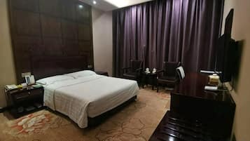A hotel room with a bed, a desk, a chair, a television, and a large window with curtains.