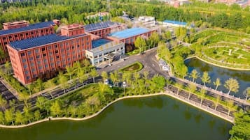 A large building complex with multiple red brick structures, a central blue-roofed building, and a surrounding landscaped area with a pond.