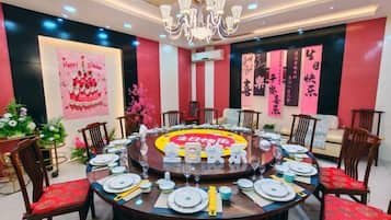 A round dining table set for a meal with chairs around it, a chandelier above, and decorative elements on the walls.