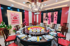 A round dining table set for a meal with chairs around it, a chandelier above, and decorative elements on the walls. - Taoyuan Hotel (Pingyuan)