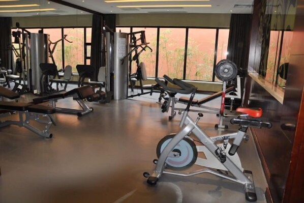 A gym with various exercise equipment, including treadmills and weight machines, and large windows offering a view of the outdoors. - Taoyuan Hotel (Pingyuan)
