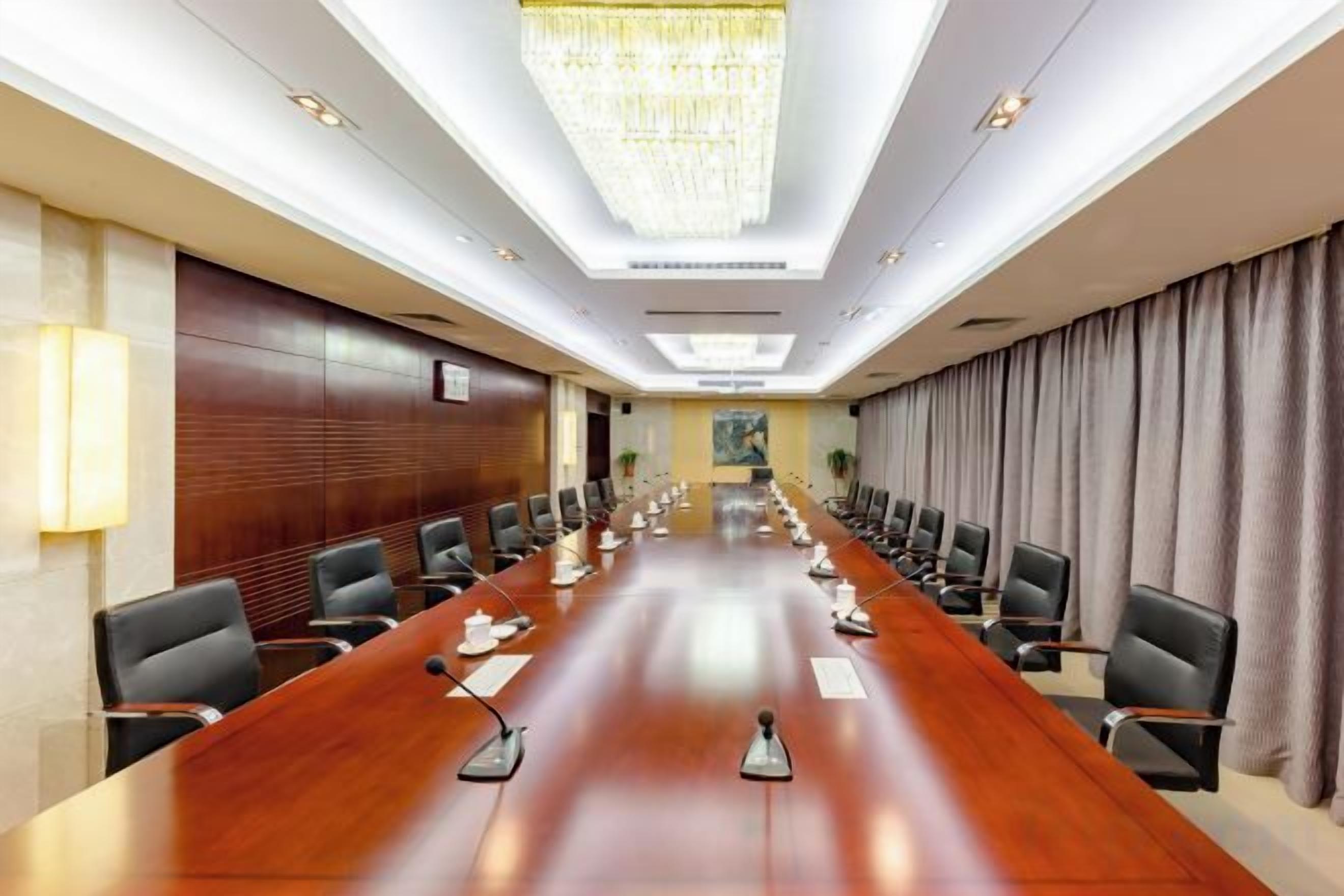 A conference room with a long table, chairs, microphones, and a chandelier.