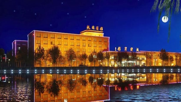 A hotel with a reflection in the water, featuring a large building with multiple floors and a prominent sign at the top.