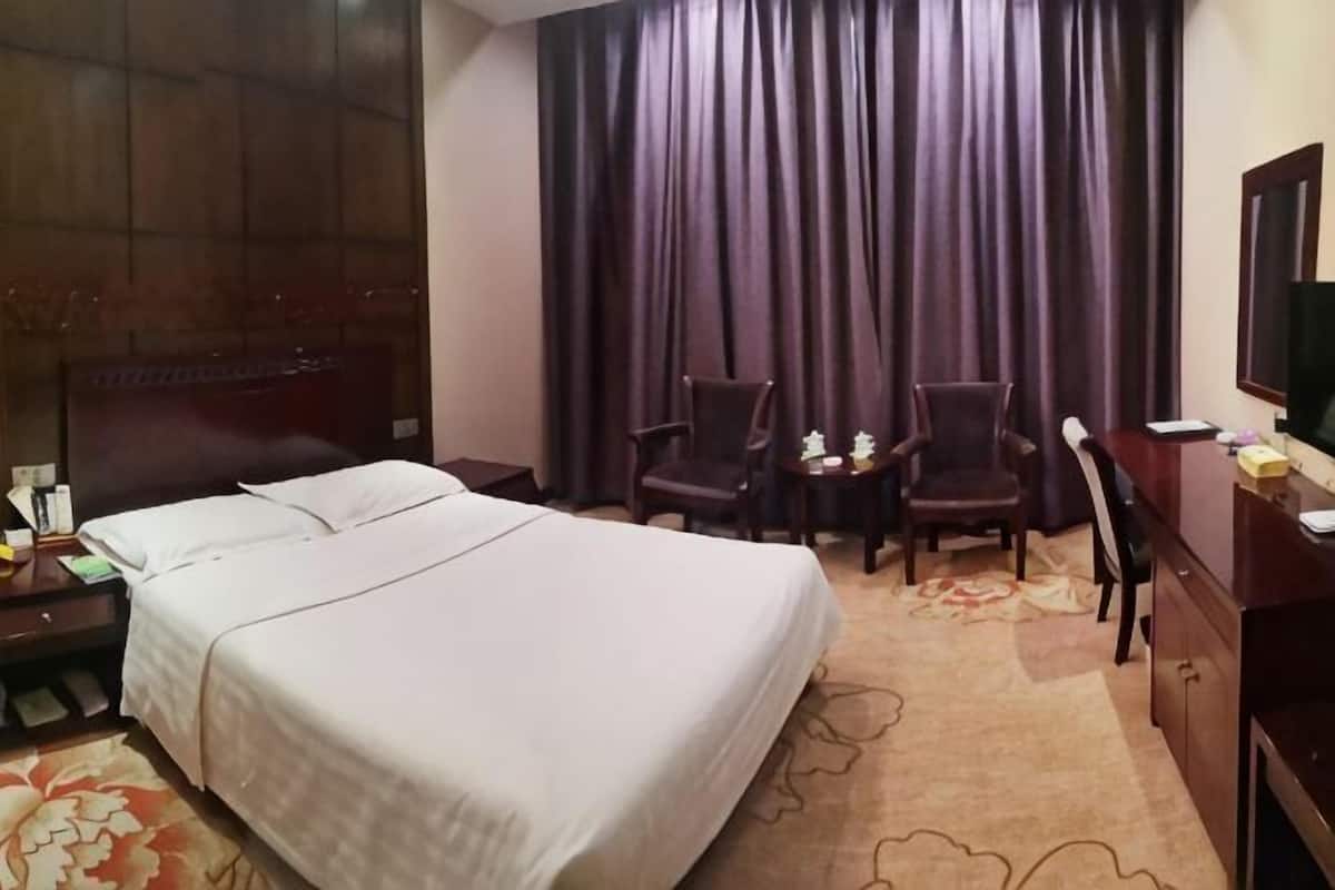 Una camera d'albergo con un letto, due poltrone, una scrivania, una televisione e una finestra con tende.