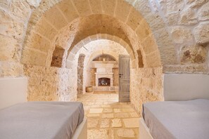 A stone-walled room with two beds, a fireplace, and an arched ceiling.