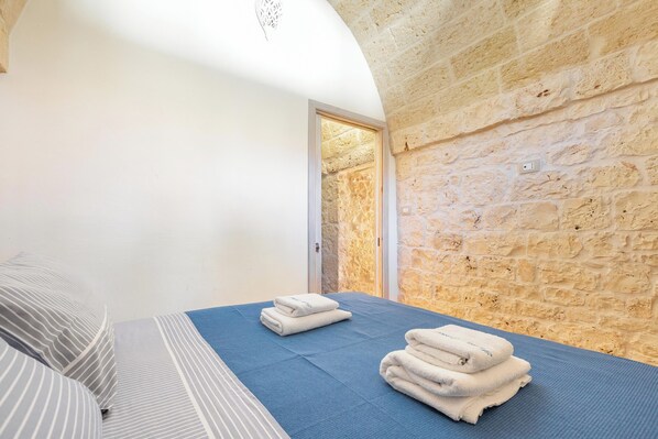 A bedroom with a stone wall, a bed with striped bedding, and towels on the bed.