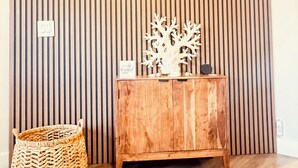 A room with a wooden slatted wall, a wooden cabinet with decorative items, and a woven basket on the floor. - The Bright Haven in Cape Coral  (Cape Coral)