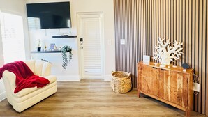 A living room with a beige sofa, a red throw blanket, a wooden cabinet, and a wall-mounted TV. - The Bright Haven in Cape Coral  (Cape Coral)