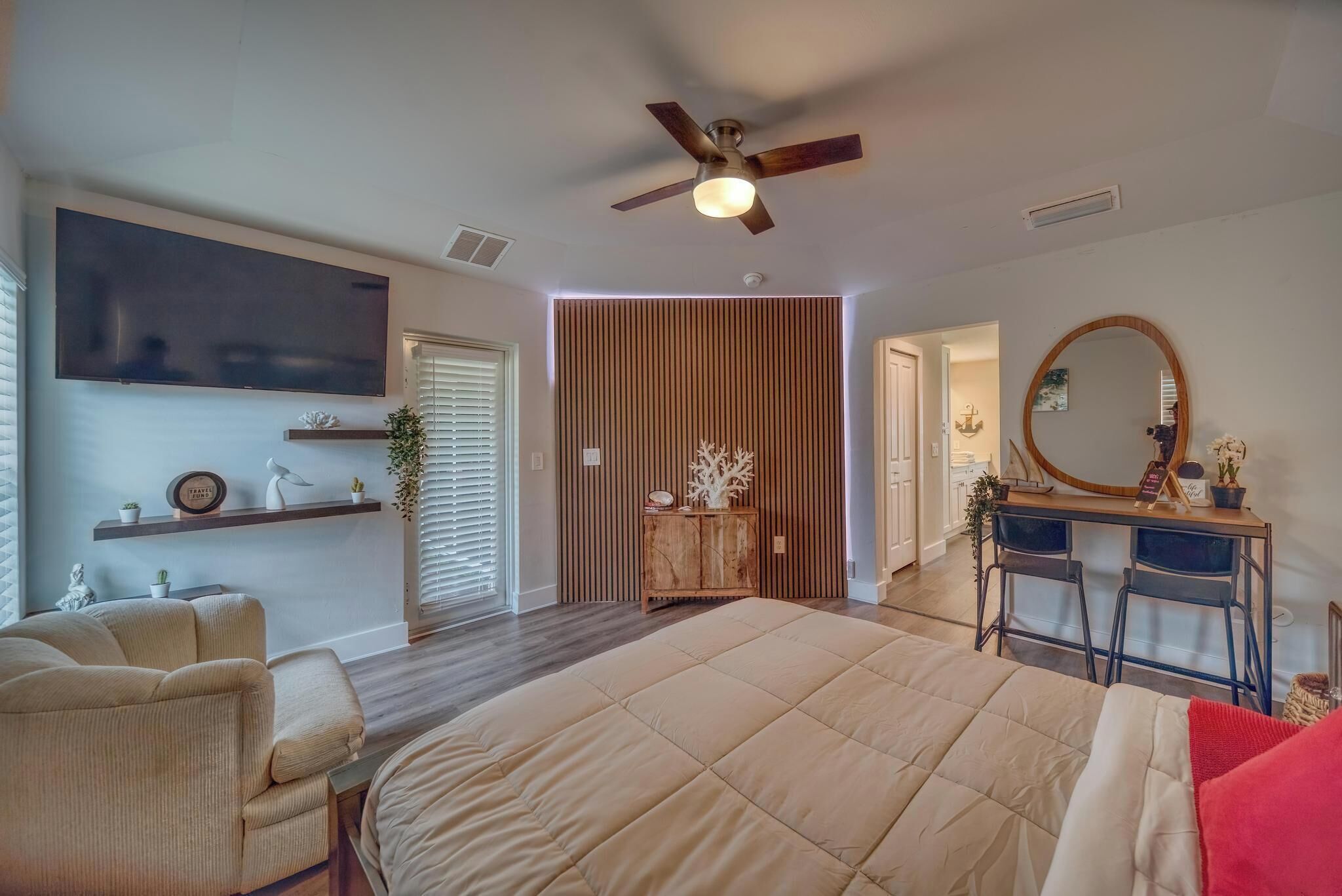 Una camera da letto con un letto grande, un ventilatore a soffitto, una TV a parete, una scrivania con due sedie e uno specchio.