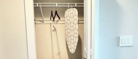 A small, enclosed closet with a wooden bench, a hanging iron board, and a coat rack.
