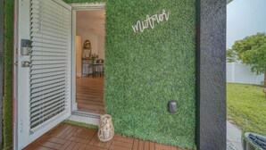 A modern entrance with a green artificial grass wall and a door with a white shutter. - The Bright Haven in Cape Coral  (Cape Coral)