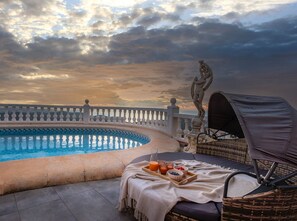 A poolside area with a chaise lounge, a table with breakfast items, and a statue. - Villa TERRACOTA by Abahana Villas (Benitachell)