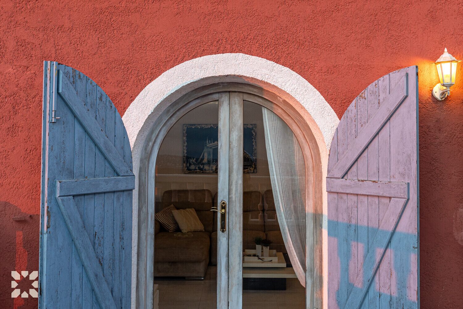 Une porte d’entrée avec deux portes en bois bleues qui donnent sur une pièce contenant un canapé et une petite table.