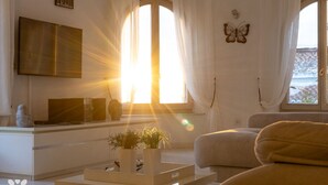 Una sala moderna con un televisor de pantalla plana, un sofá, una mesa de centro con plantas y un ventanal con cortinas.
