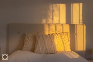 Ein Bett mit Kopfteil, drei Kissen und ein Fenster, das ein warmes Licht wirft.