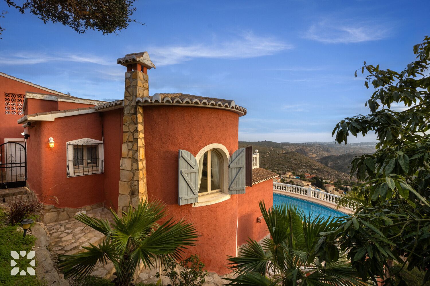 A villa with a stone chimney, a pool, and a view of the hills.