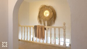 Un escalier avec une balustrade blanche, une tapisserie murale tissée et un plaid beige drapé sur la rambarde.