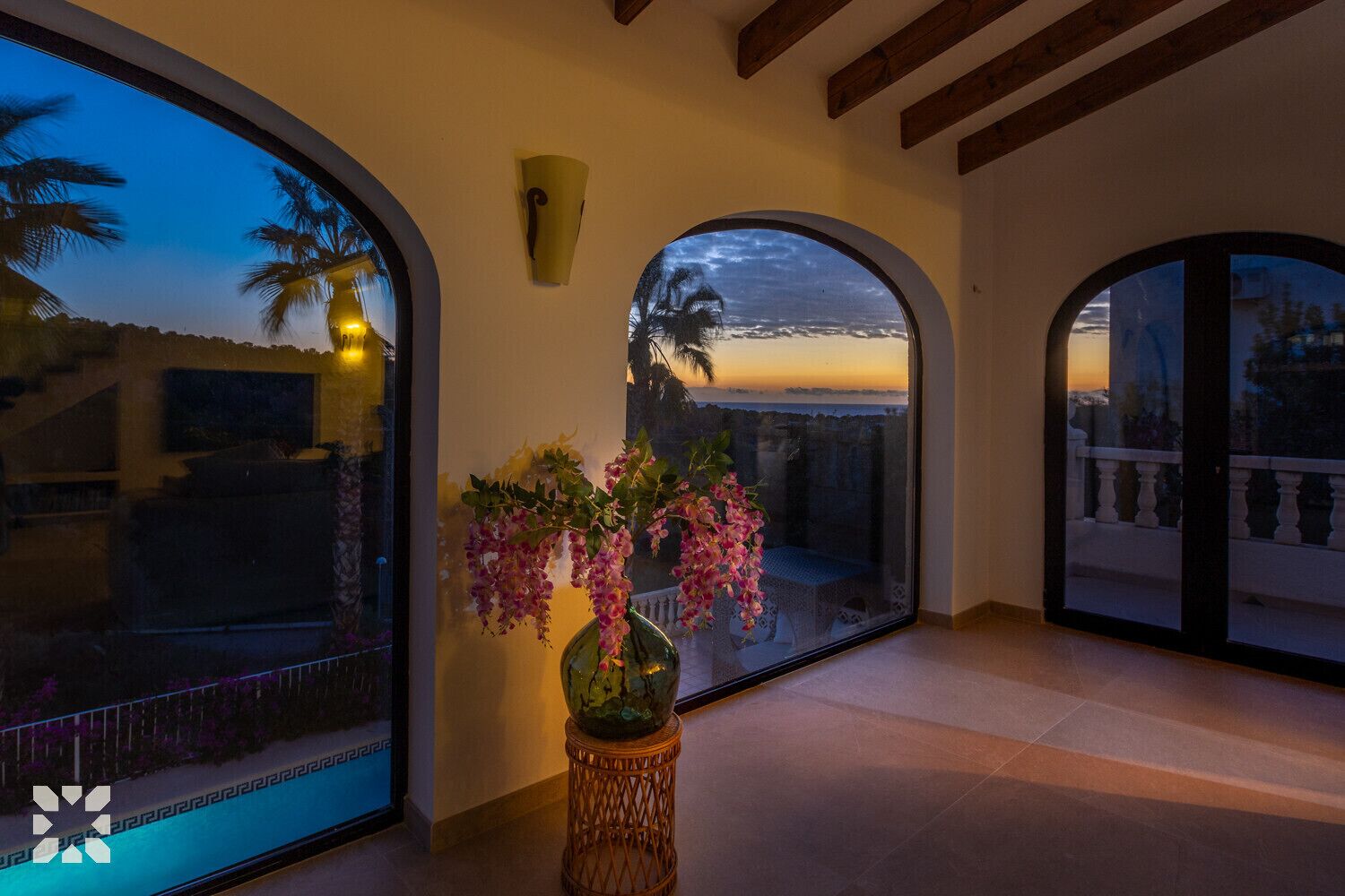 A spacious room with large arched windows offering a view of the sunset and palm trees.
