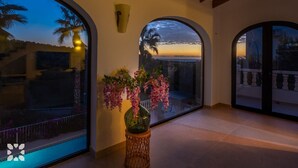 Une pièce spacieuse dotée de grandes fenêtres en arc qui offrent une vue sur le coucher de soleil et les palmiers.
