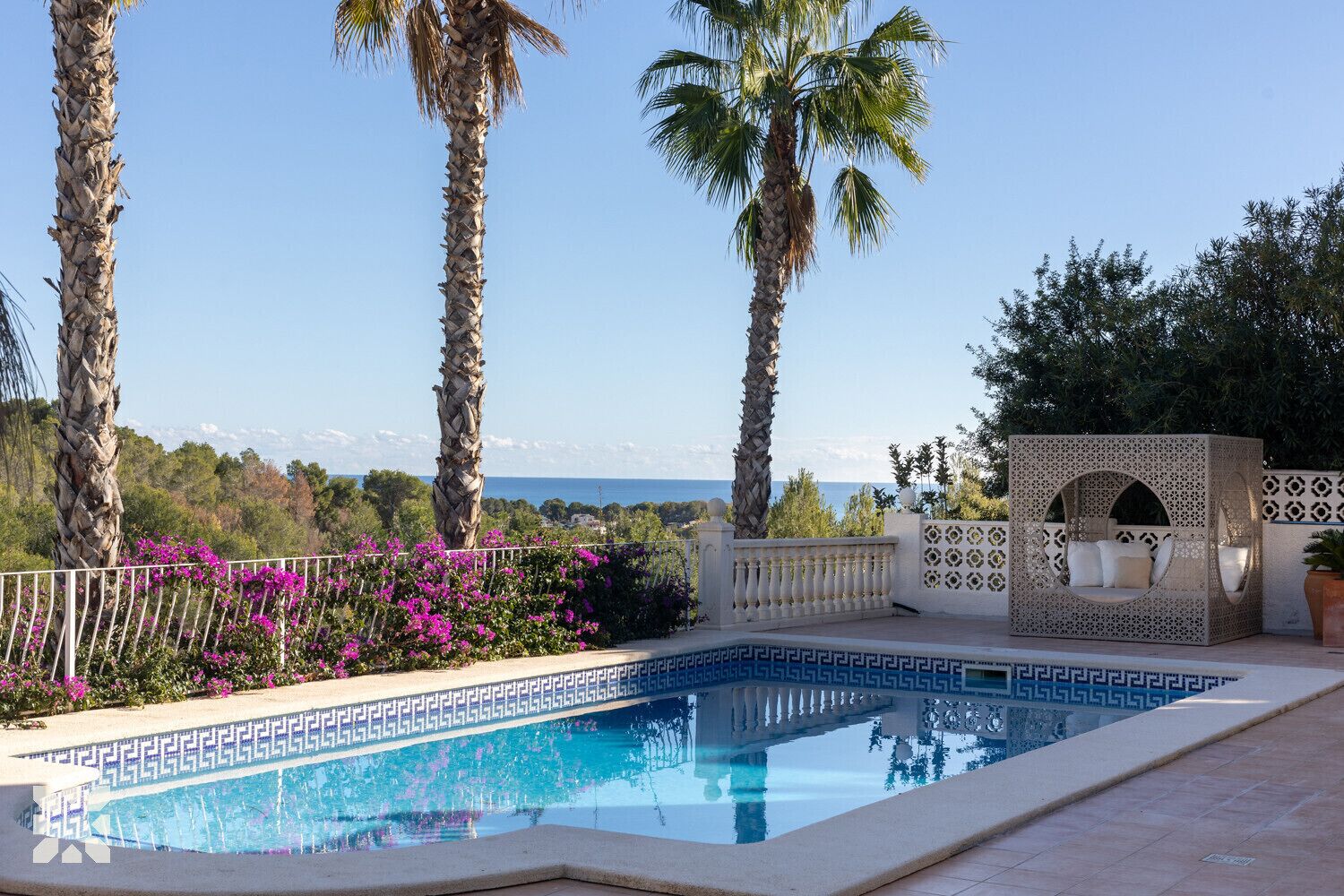 Une piscine avec vue sur la mer, entourée de palmiers et de fleurs violettes.