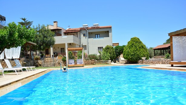 Una piscina con lettini, una zona relax coperta e un edificio con tetto in tegole rosse.