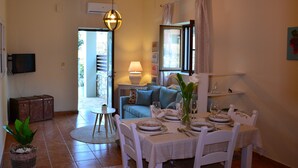 Zona pranzo con tavolo imbandito per quattro, divano, lampada e televisore a parete.