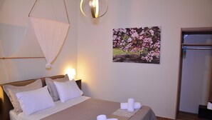 Un letto rifatto con cuscini, un lampadario a parete, un quadro con fiori e una porta con porta asciugamani.