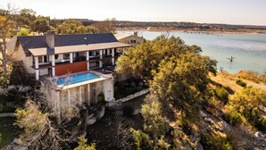 Une maison avec une piscine, entourée d’arbres et bordée par un plan d’eau.
