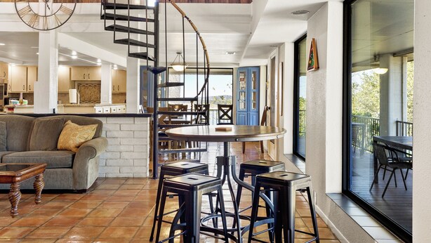 Une cuisine moderne dotée d’un îlot central, d’un coin repas avec une table ronde et des tabourets de bar, d’un escalier menant à un niveau supérieur et de grandes fenêtres offrant une vue sur l’extérieur.