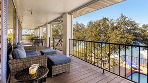 Une terrasse extérieure couverte, aménagée avec des meubles en osier, une table avec une tasse et une vue sur une piscine et des arbres.