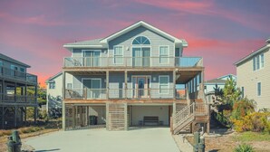 A two-story beachfront house with a balcony, a covered entryway, and a staircase leading to the upper level.