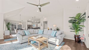 A spacious living room with a grey sectional sofa, a wooden coffee table, and a large potted plant.