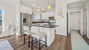 A modern kitchen with white cabinets, a central island with bar stools, stainless steel appliances, and pendant lighting.