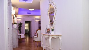 Un pasillo con un espejo blanco ornamentado, una consola blanca con adornos y dos sillones tapizados en blanco.