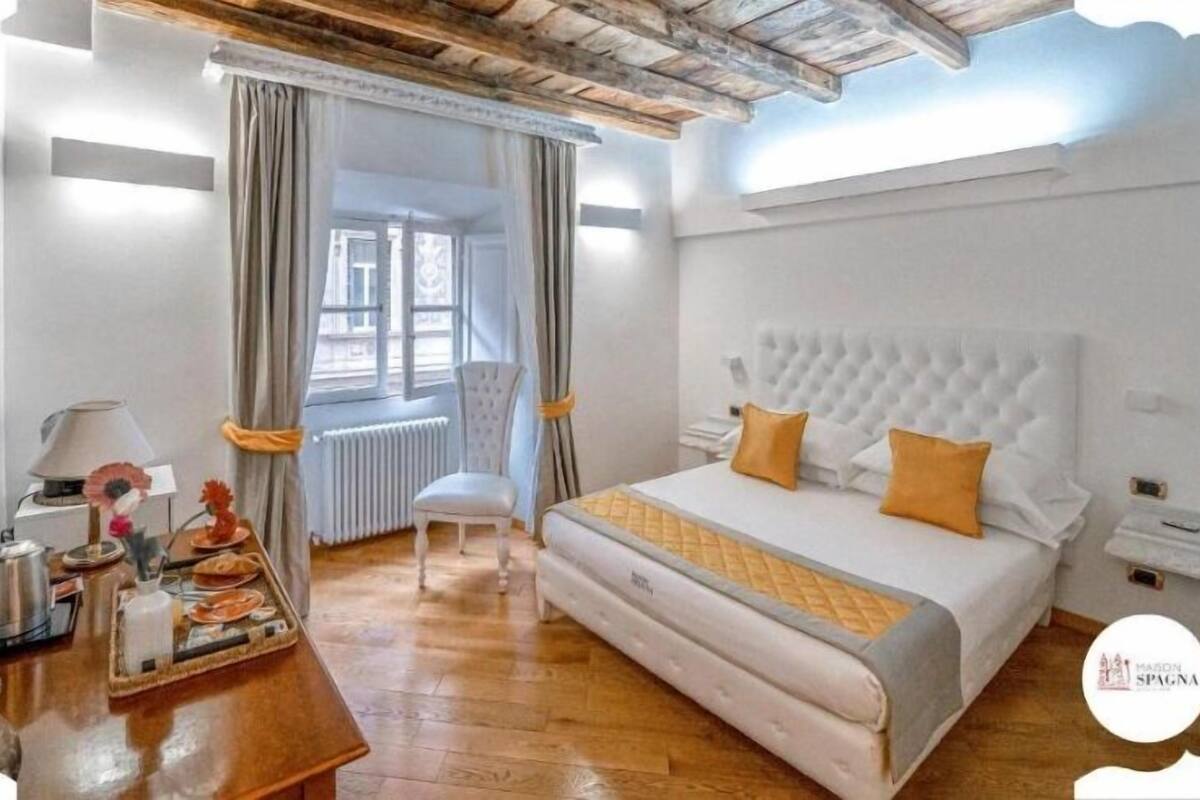 A hotel room with a large bed, a chair, a desk with a lamp, and a window with curtains.