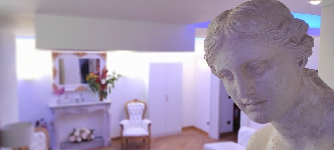 A room with a white fireplace, a white chair, and a statue.