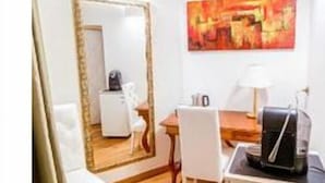Una habitación pequeña con suelo de madera, un escritorio blanco, una silla, un espejo grande y un cuadro en la pared.
