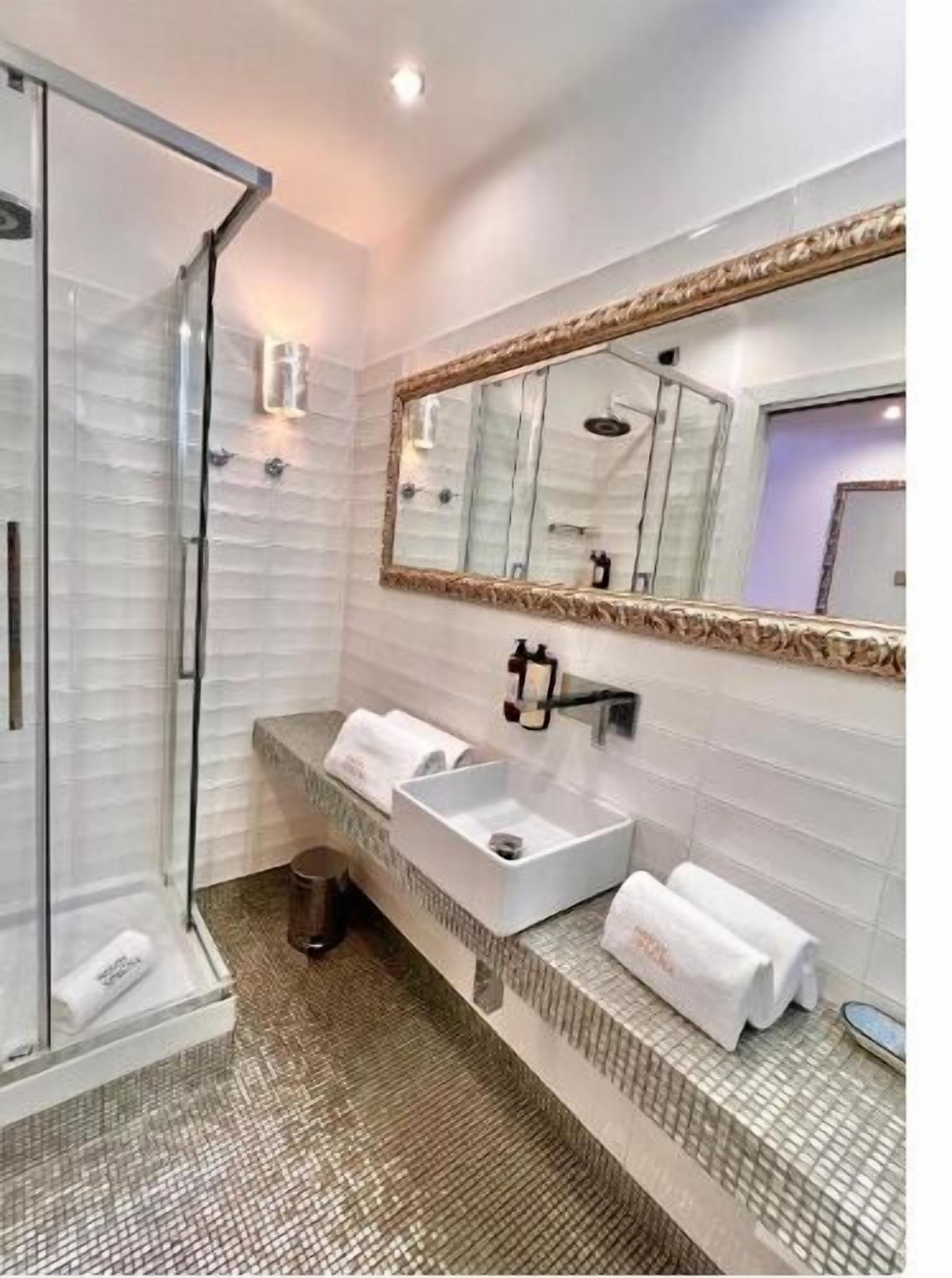 A modern bathroom with a glass shower enclosure, a large mirror, and a white sink with two towel dispensers.