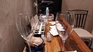 Une table à manger avec deux verres à vin, un plateau sur lequel reposent deux tasses noires et une bouteille d’eau.