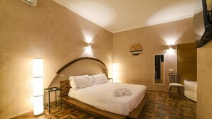 Une chambre d’hôtel avec un grand lit, deux lampes fixées au mur, une petite table, une chaise et une salle de bain avec une baignoire.