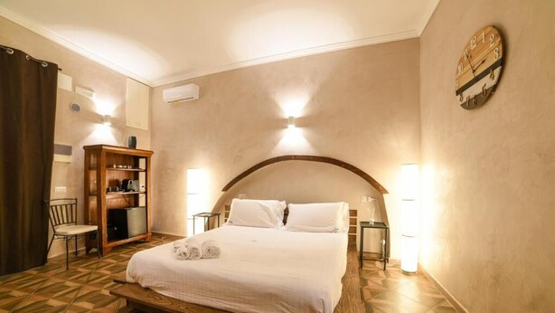 Une chambre d’hôtel avec un lit, une armoire en bois, une chaise et une horloge murale.