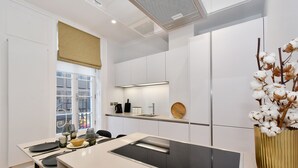 A modern kitchen with white cabinetry, a central island with a built-in stove, a window with blinds, and a vase with dried flowers on the right. - Albemarle Elegance I - 37as1 (London)